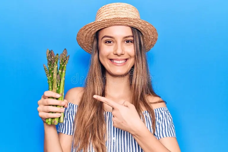 jovencita hermosa con sombrero sosteniendo esparragos sonriendo feliz senalando la mano y el dedo 227101330 - Аспарагус